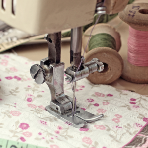 Close-up of a sewing machine stitching floral fabric with colorful thread spools nearby.