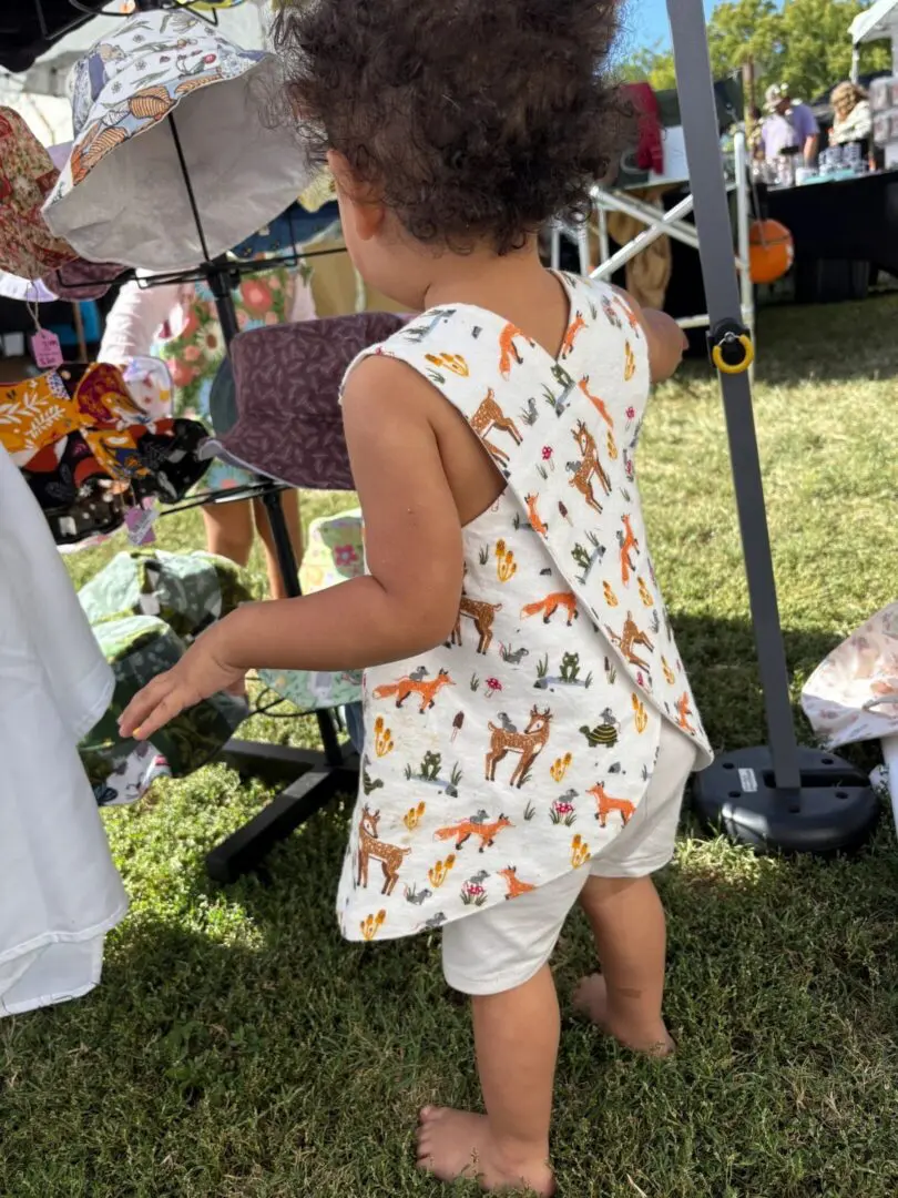 A toddler wearing a butterfly-patterned dress outdoors.